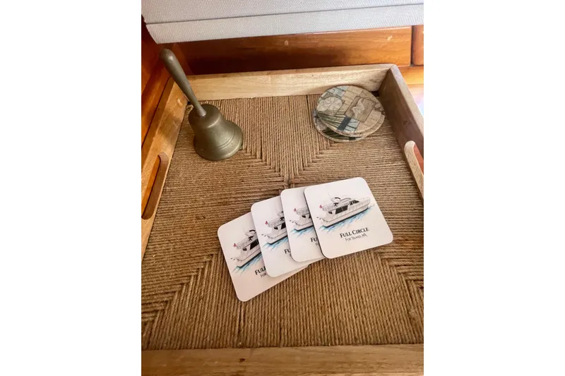 Slide: The Image of Coasters featuring Canoe Cove 50 Pilothouse Yacht, 2002, on a woven tray with a brass bell. - 24