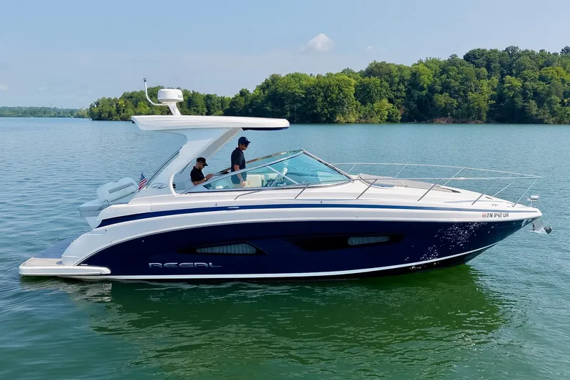 Slide: The Image of 2021 Regal 33 Express boat cruising on a serene lake with lush green shoreline. - 14