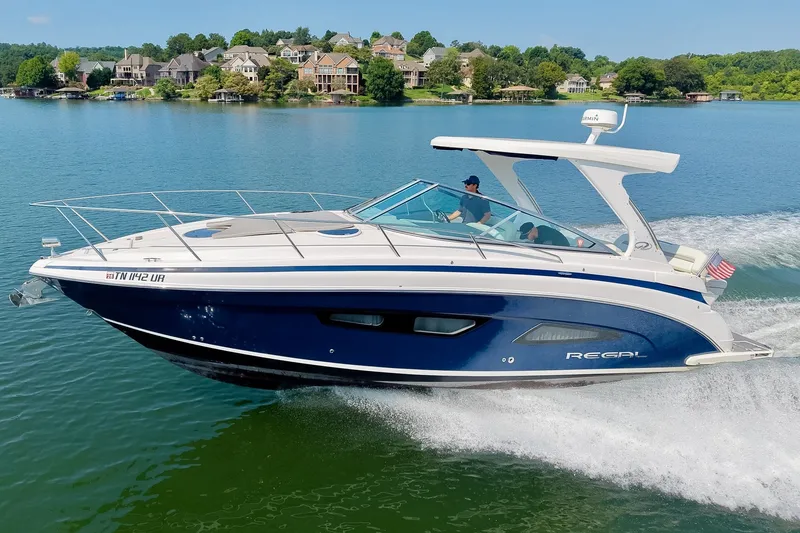 The Image of 2021 Regal 33 Express boat cruising on a scenic lake with waterfront homes. - 0