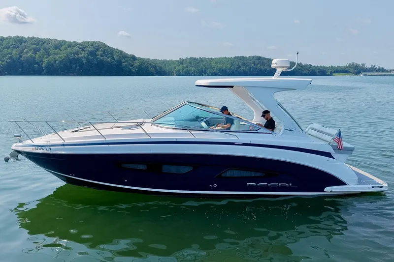 Slide: The Image of 2021 Regal 33 Express boat cruising on a serene lake with lush green hills. - 15