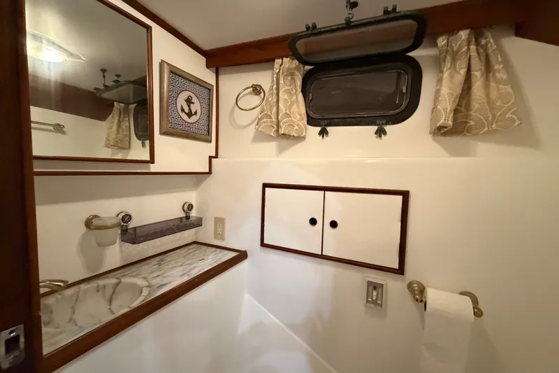 Slide: The Image of 1983 CHB Sedan Trawler bathroom with marble countertop, nautical decor, and porthole window. - 19