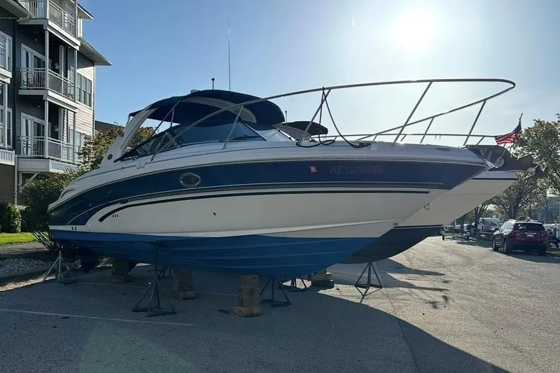 The Image of 2001 Sea Ray 290 Sun Sport boat on stands, parked near residential buildings. - 0