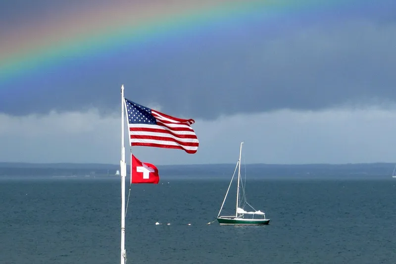 Slide: The Image of Sailboat Alerion Express 20 (1998) on lake with rainbow and flags in background. - 7
