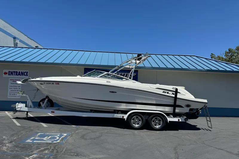 Slide: The Image of 2007 Sea Ray SLX 250 boat on trailer, parked outside a building with blue roof. - 0