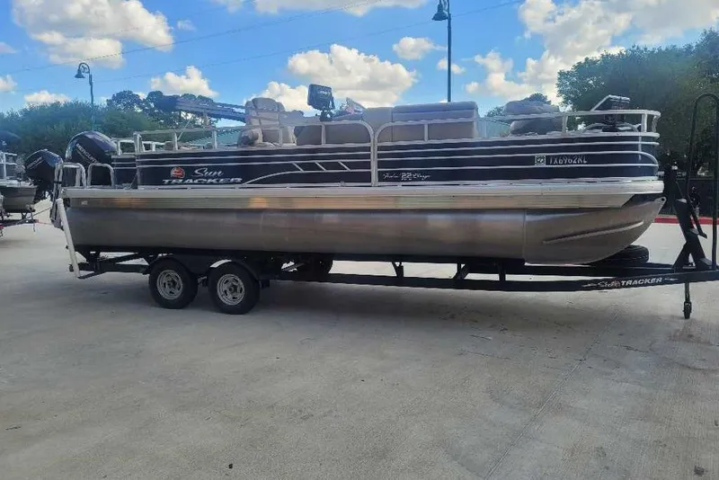 The Image of 2022 Sun Tracker Fishin' Barge 22 DLX pontoon boat on trailer, parked outdoors. - 0