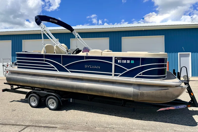Slide: The Image of 2018 Sylvan 8522 Mirage Fish pontoon boat on trailer, parked outside blue building. - 1