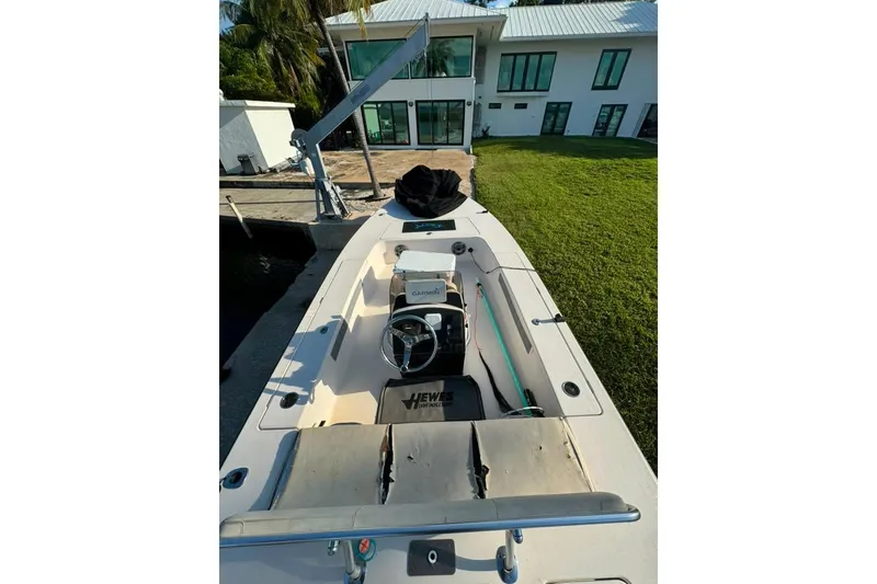 Slide: The Image of 2003 Hewes Redfisher 21 boat docked near a modern house, showcasing interior and steering wheel. - 5