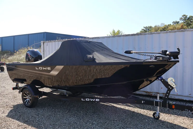 Slide: The Image of 2027 Lowe Fishing Machine 1875 boat with cover, parked on a trailer outdoors. - 44