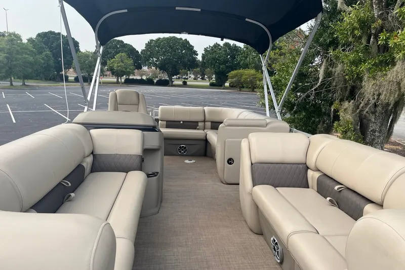 Slide: The Image of 2025 Sun Tracker Party Barge 20 DLX interior with beige seating and canopy in parking lot. - 6