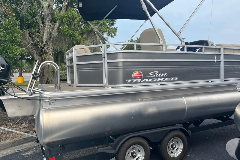 Slide: The Image of 2025 Sun Tracker Party Barge 20 DLX pontoon boat on trailer, parked outdoors. - 2