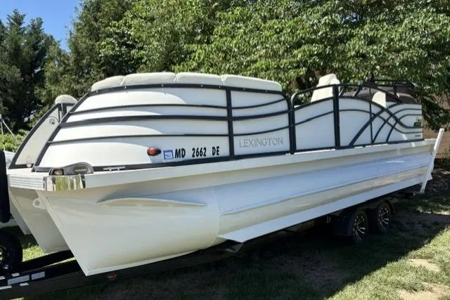 The Image of 2022 Lexington 623 pontoon boat on trailer, parked outdoors with trees in background. - 1
