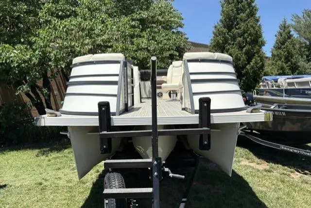 Slide: The Image of 2022 Lexington 623 pontoon boat on trailer, parked on grass with trees in background. - 2