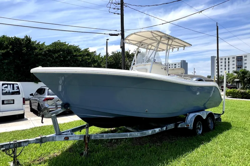 Slide: The Image of 2019 Cobia 220 Center Console boat on trailer, parked on grass under blue sky. - 2