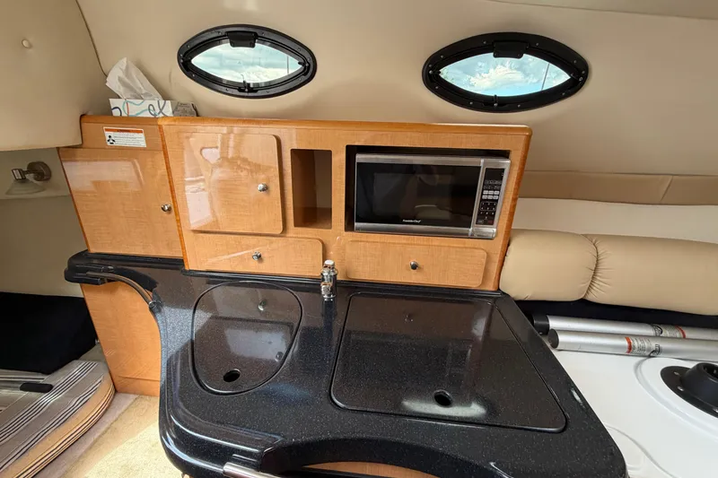 Slide: The Image of 2015 Glastron GS 289 boat interior with kitchenette, featuring microwave and sink. - 16