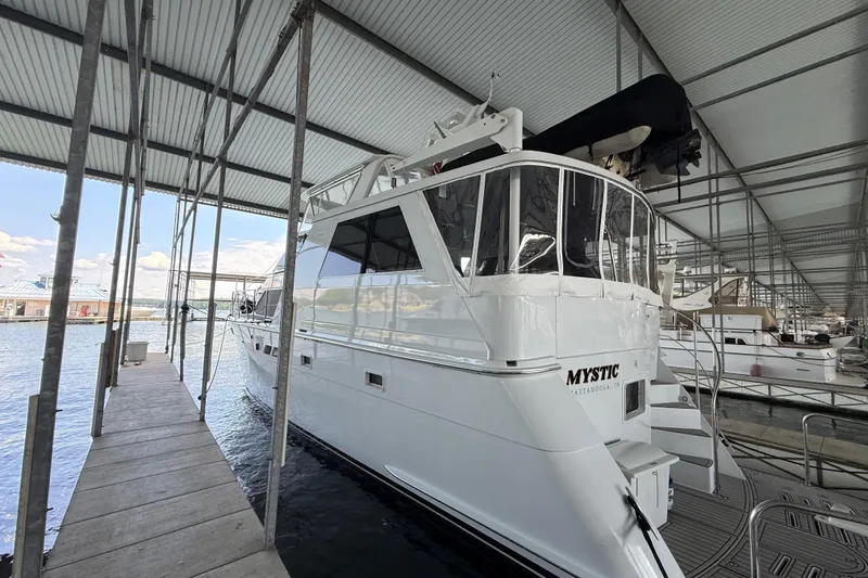 Slide: The Image of 1998 Hatteras yacht docked in marina, featuring sleek white design and spacious deck area. - 4