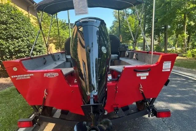 Slide: The Image of 2026 Tracker Pro Guide V-16 SC boat, red exterior, parked outdoors, rear view with motor. - 3