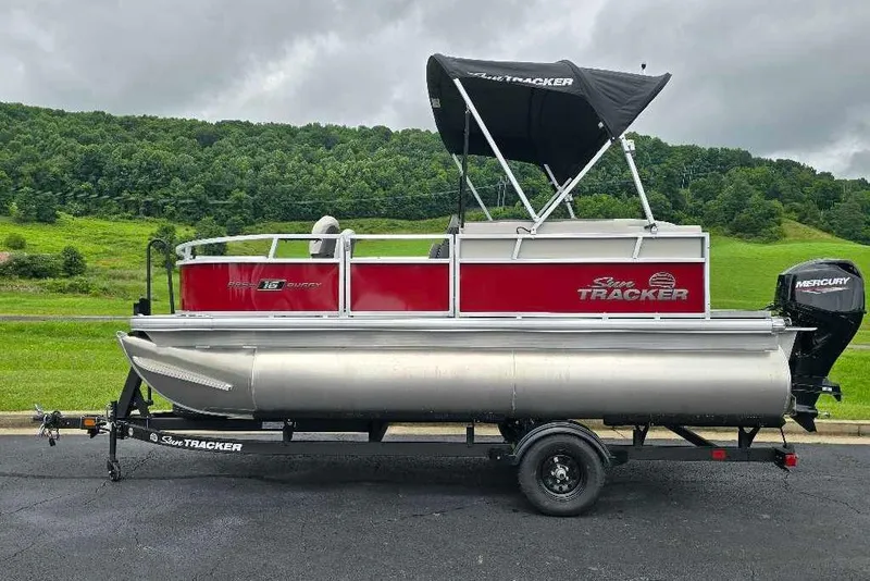 Slide: The Image of 2026 Sun Tracker Bass Buggy 16 XL Select pontoon boat on trailer, scenic background. - 1