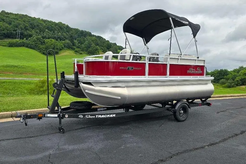 Slide: The Image of 2026 Sun Tracker Bass Buggy 16 XL Select pontoon boat on trailer, scenic background. - 7
