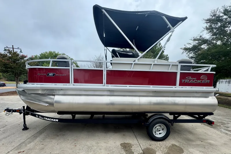 The Image of 2026 Sun Tracker Bass Buggy 18 DLX pontoon boat on trailer, red and silver design. - 0