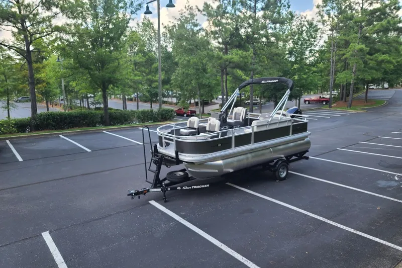 Slide: The Image of 2026 Sun Tracker Bass Buggy 18 DLX pontoon boat in a parking lot, surrounded by trees. - 15