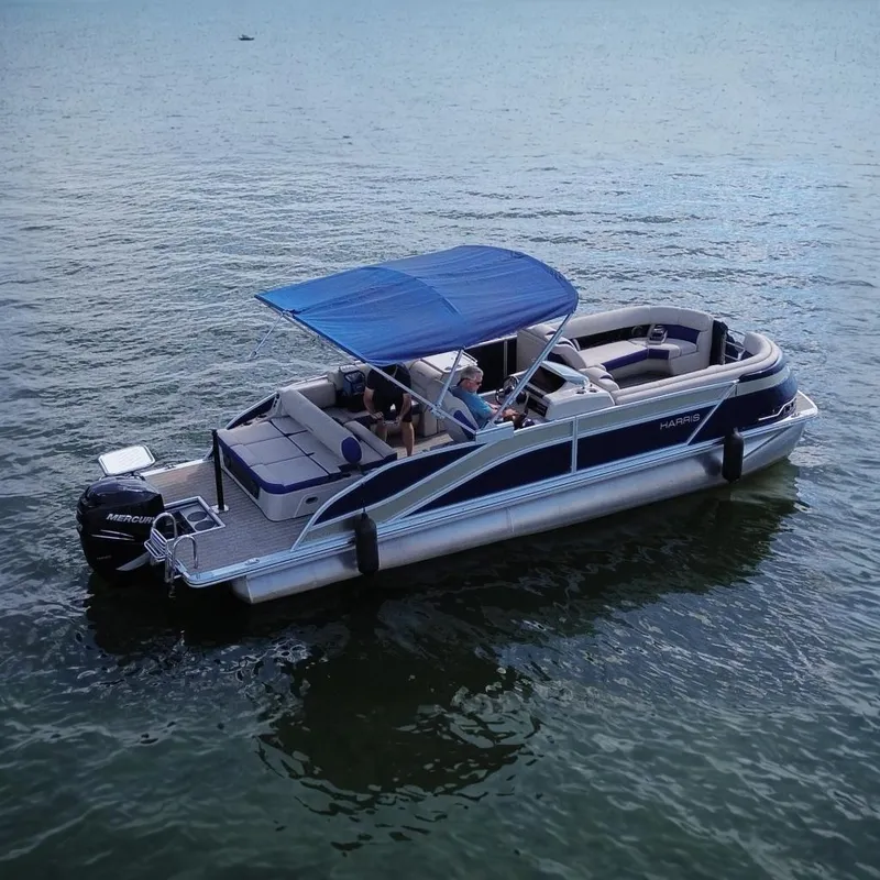 The Image of 2022 Harris Grand Mariner 250 pontoon boat with blue canopy on calm water. - 0