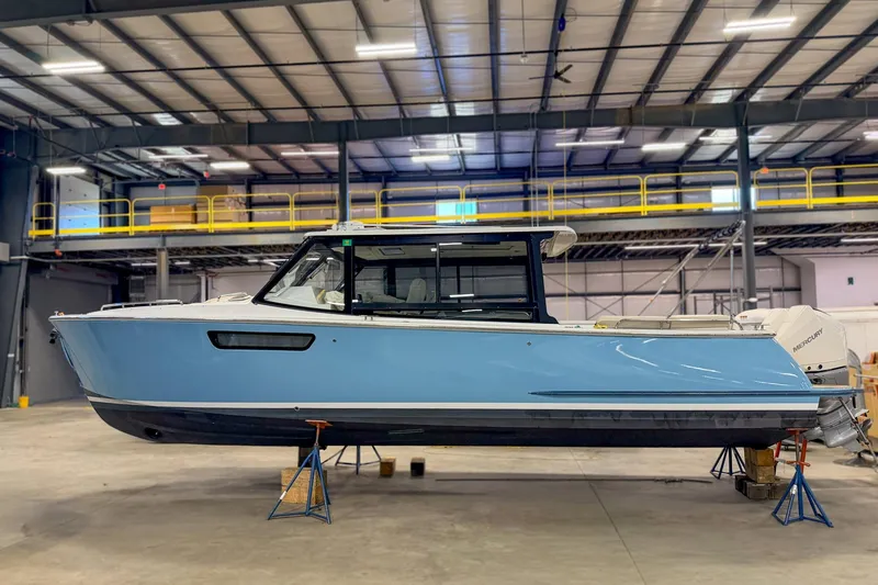 The Image of 2022 MJM 3 boat in a warehouse, displayed on stands, with a sleek blue hull. - 0