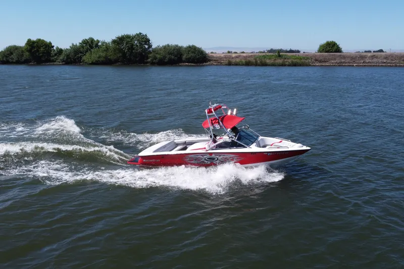 The Image of Red 2004 Master Craft 210 boat cruising on a lake with lush greenery in the background. - 1