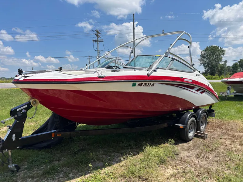 The Image of A red 2014 Yamaha AR210 boat on a trailer, parked on grass. - 0