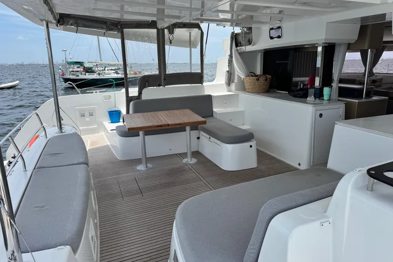 Slide: The Image of Spacious deck of 2025 Lagoon 46 catamaran with seating and table, docked by the sea. - 16