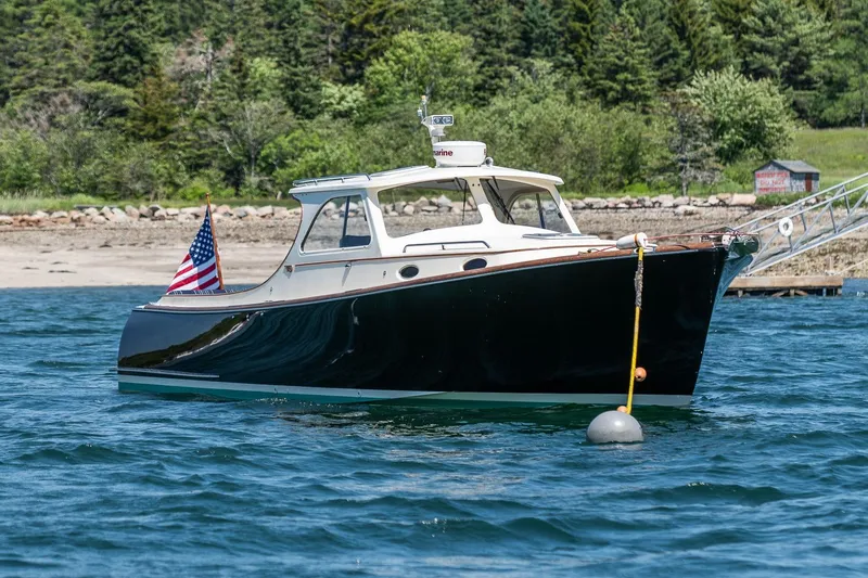 The Image of 2001 Hinckley Picnic Boat 36 Classic on water, with American flag, near wooded shoreline. - 0