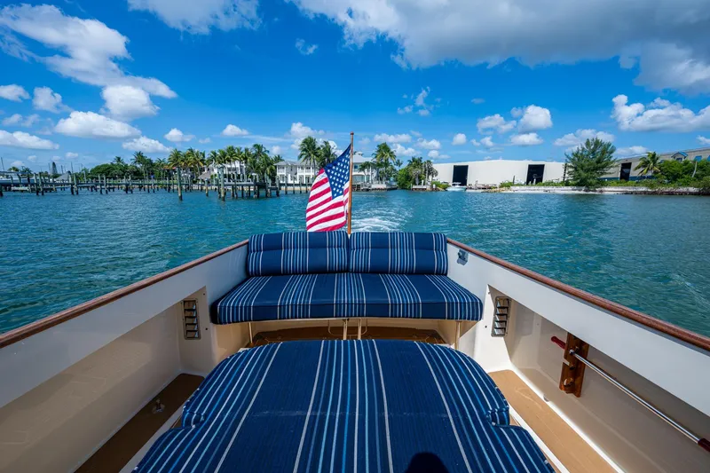 Slide: The Image of 2001 Hinckley Picnic Boat Classic cruising with American flag, blue striped seating, and scenic waterfront. - 23