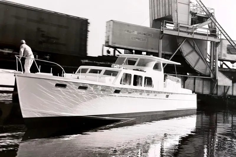Slide: The Image of 1967 Huckins Linwood 53 yacht cruising near industrial structures on calm water. - 2