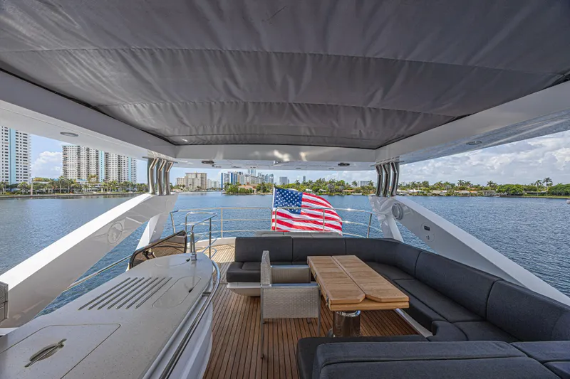 Slide: The Image of Luxurious 2017 Sunseeker 75 Yacht deck with seating, table, and American flag, overlooking waterfront cityscape. - 19