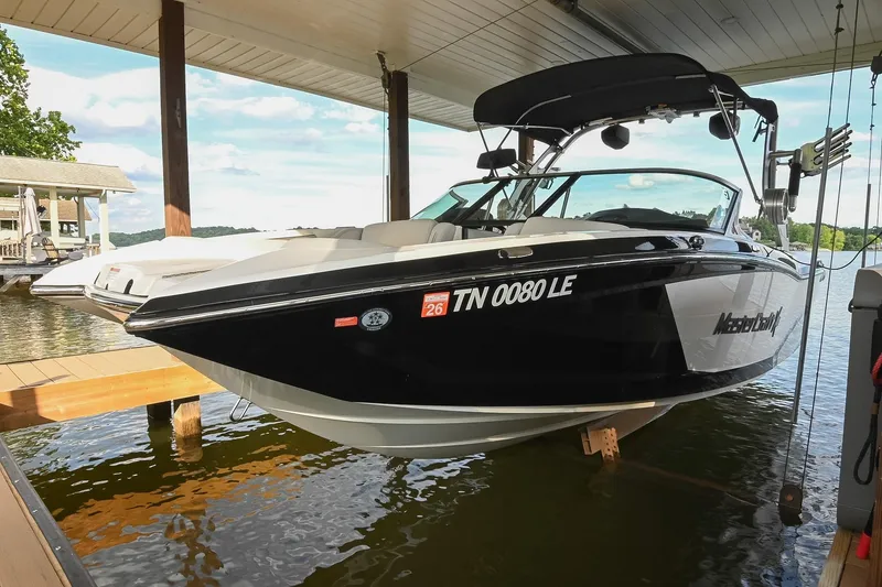 The Image of 2018 MasterCraft X23 boat docked under a covered slip on a sunny day. - 0
