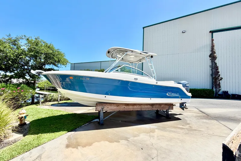 Slide: The Image of 2012 Robalo R247 Dual Console boat on display outdoors, blue and white design. - 2