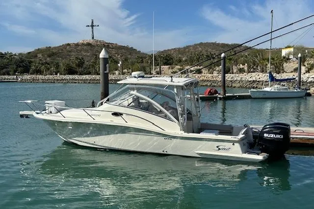 Slide: The Image of 2008 Scout 295 Abaco boat docked in a serene marina with scenic hills. - 2
