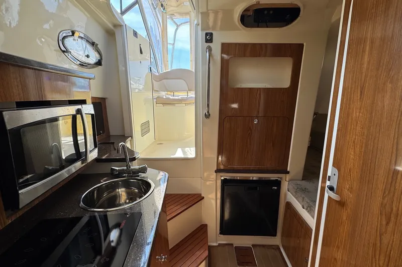 Slide: The Image of 2008 Scout 295 Abaco boat interior with kitchenette, featuring microwave, sink, and wooden cabinetry. - 27