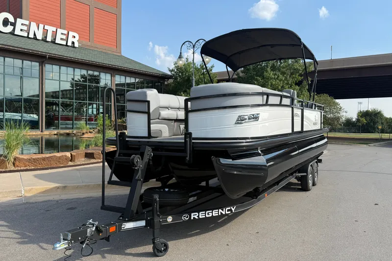 Slide: The Image of 2024 Regency 250 DL3 pontoon boat on trailer outside a showroom. - 2
