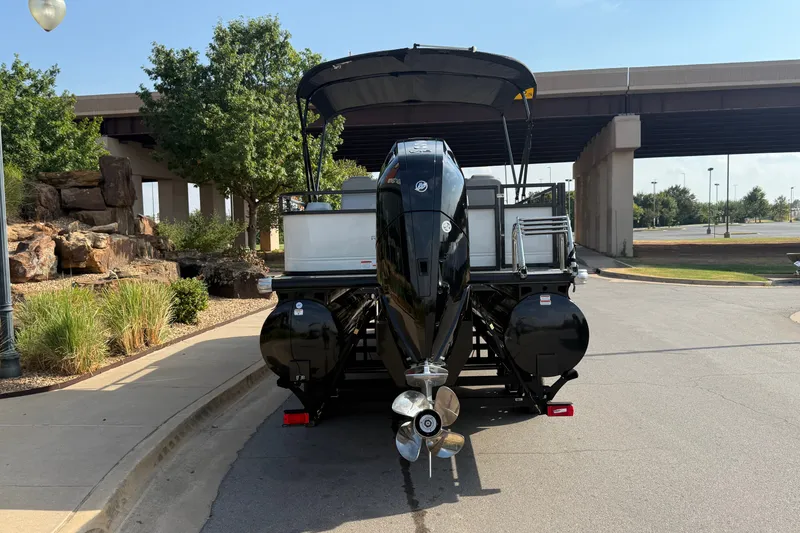 Slide: The Image of 2024 Regency 250 DL3 pontoon boat with powerful outboard motor, parked near a bridge. - 13