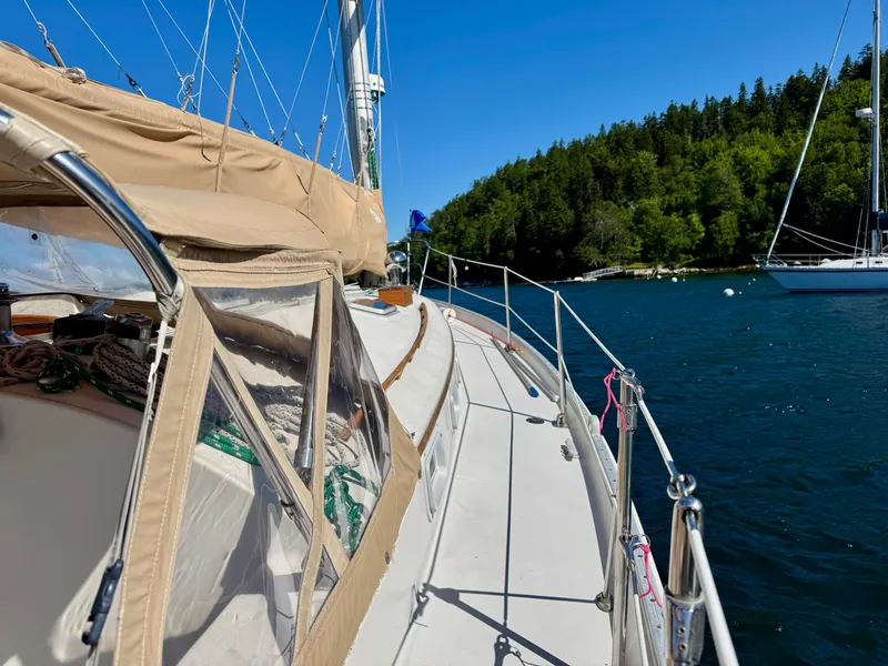 Slide: The Image of 1989 Nonsuch 30 Ultra sailboat on serene water near lush green shoreline. - 21