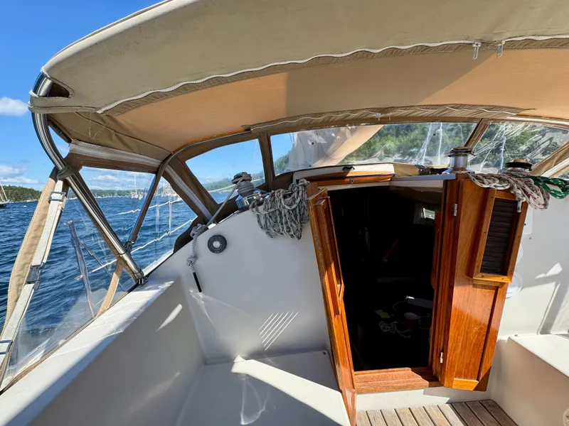 Slide: The Image of 1989 Nonsuch 30 Ultra sailboat cockpit with open cabin door, under sunny skies. - 26