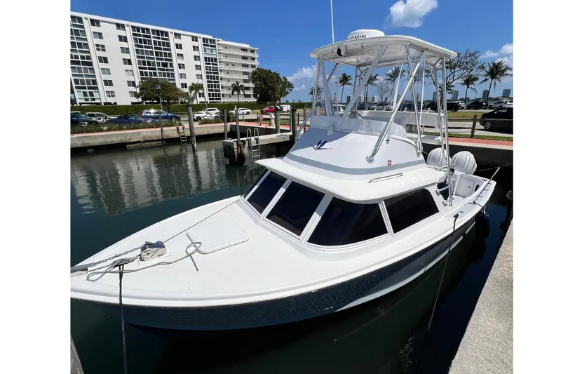 The Image of 1973 Bertram 31 Flybridge Cruiser docked in marina, clear sky, modern buildings in background. - 1