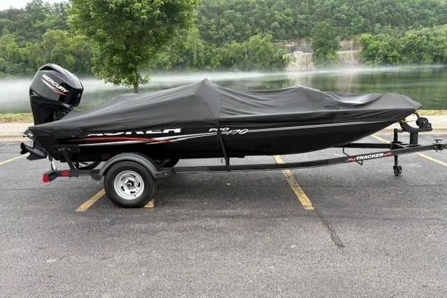 Slide: The Image of 2023 Tracker Pro 170 boat covered, parked near a scenic lake with lush greenery. - 42