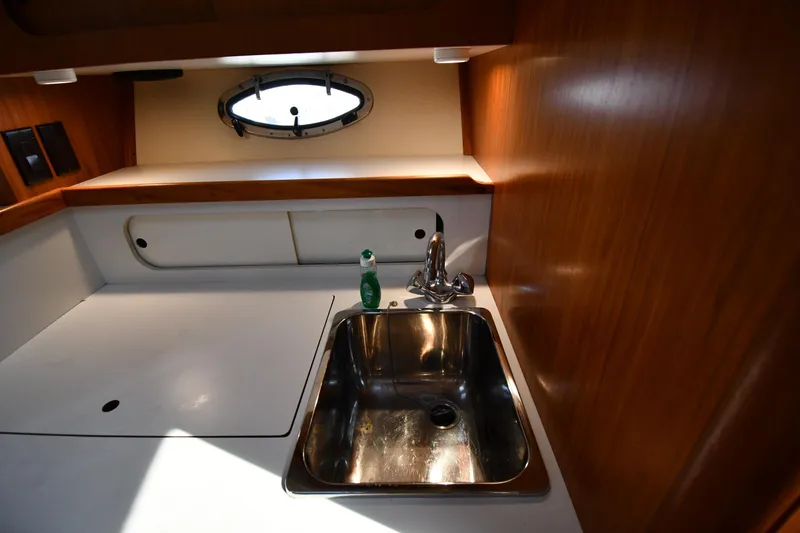 Slide: The Image of 1998 Tiara Yachts 3100 Open galley with sink, wooden cabinetry, and porthole window. - 27