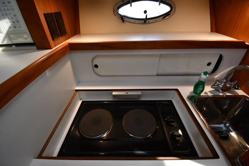 Slide: The Image of 1998 Tiara Yachts 3100 Open galley with stove, sink, and porthole window. - 28