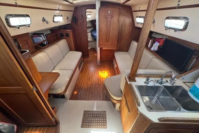 Slide: The Image of Interior of a 1997 Island Packet 37 sailboat, featuring cozy seating and a compact kitchen area. - 15
