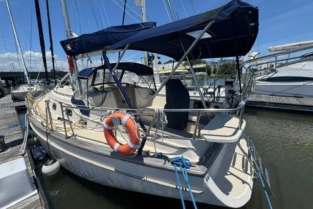 Slide: The Image of 1997 Island Packet 37 sailboat docked, featuring blue canopy and lifebuoy on deck. - 6
