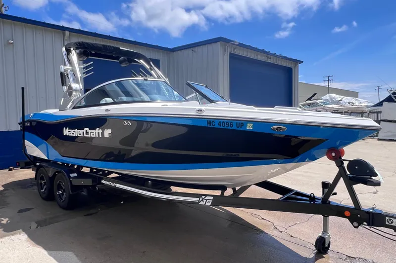 Slide: The Image of 2021 MasterCraft XT23 boat on trailer, parked outside a warehouse under a blue sky. - 2