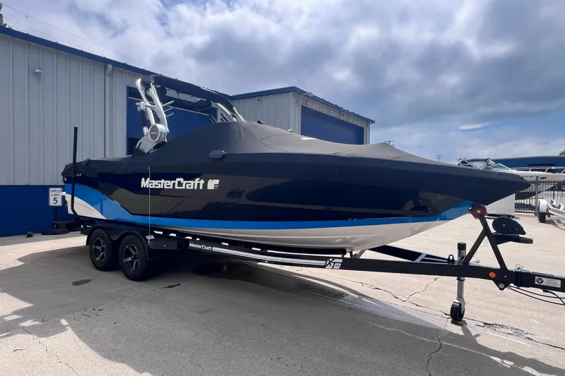 Slide: The Image of 2021 MasterCraft XT23 boat on trailer, parked outside a building under cloudy sky. - 21