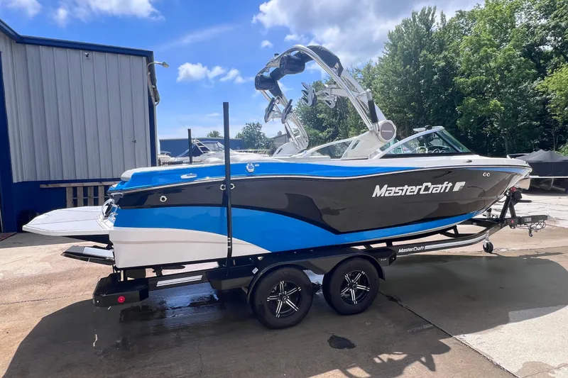 Slide: The Image of 2021 MasterCraft XT23 boat on trailer, blue and black design, parked outdoors. - 4